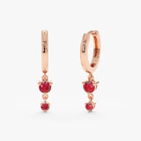 Pair of solid 14k rose gold hoop huggies with two drop down hanging rubies