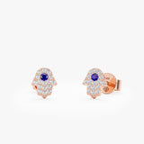 handcrafted pair of solid 14k rose gold hamsa hand stud earrings with natural diamonds and single blue sapphire