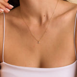 Model wearing a gold lowercase initial necklace with a diamond accent, layered with other delicate chains.