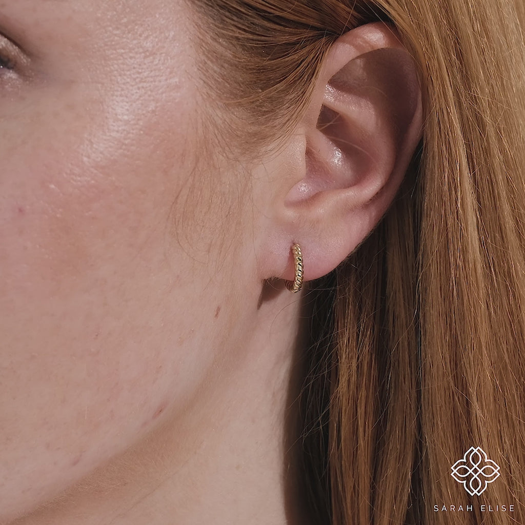 Video close up of model wearing handmade elegant solid gold twisted hoop huggie. 