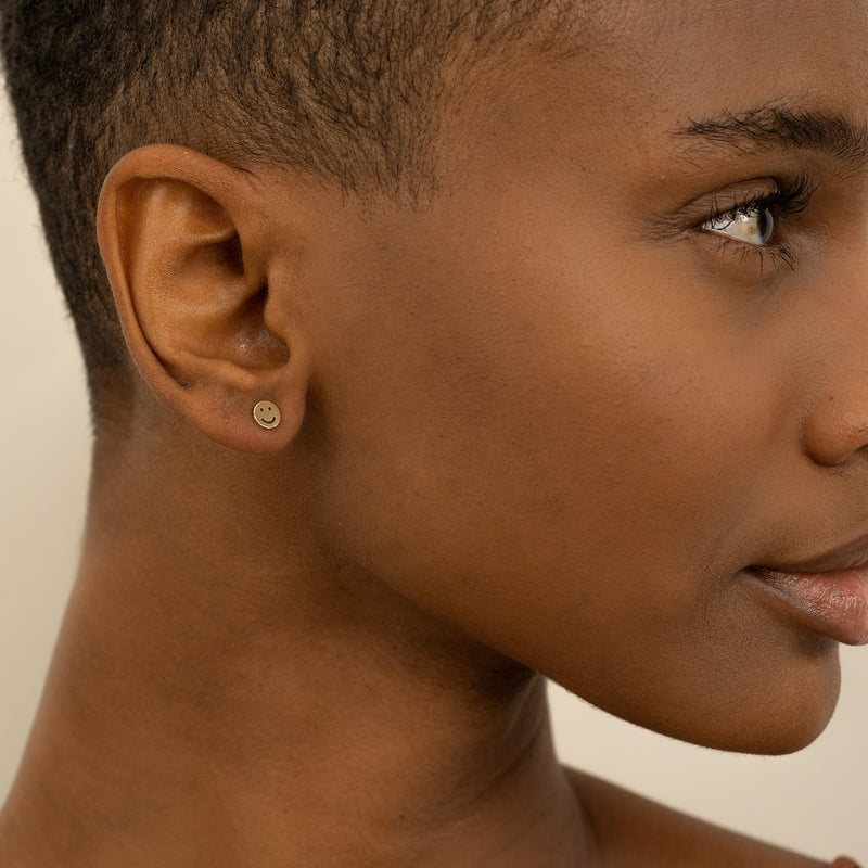 Model wears Tiny Happy Face Earring stud in solid gold